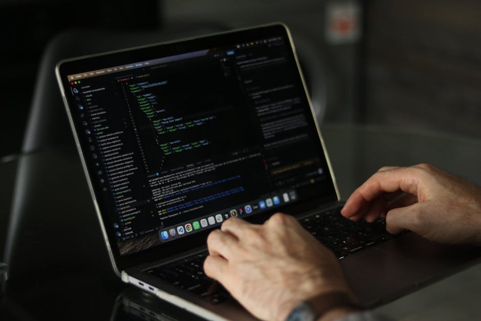 A close-up of a laptop computer on a desk displaying a software development environment with colored syntax-highlighted code on the left side and a large, orange calculator interface with black and wh